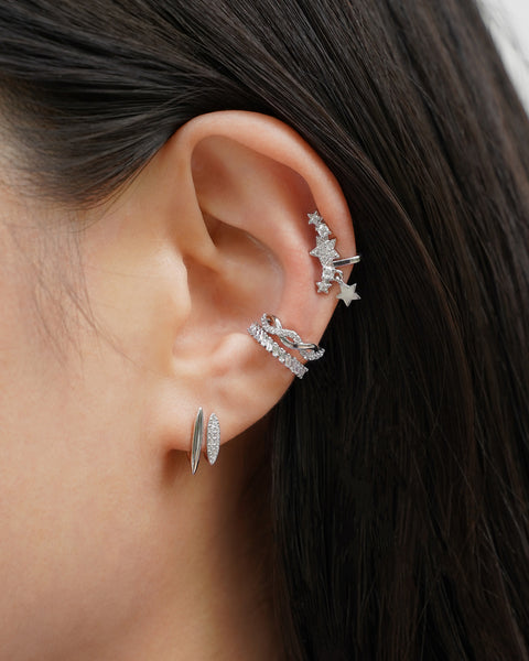 Close-up of a model's ear wearing multiple silver star-shaped earrings and diamond studded ear cuffs
