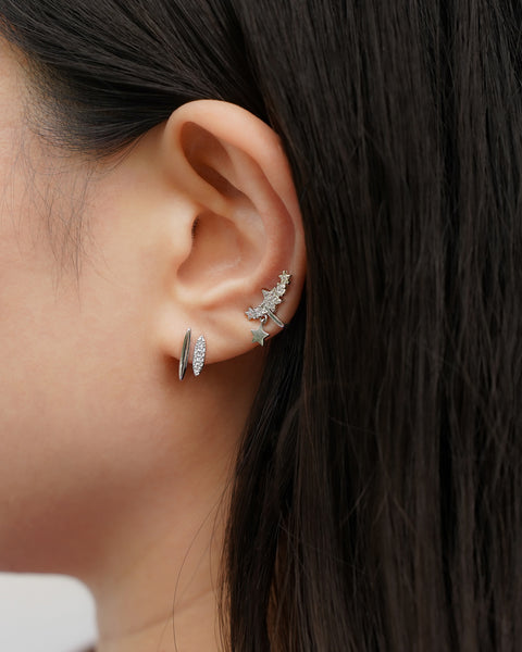 Close-up of an ear wearing two silver earrings with a dark background